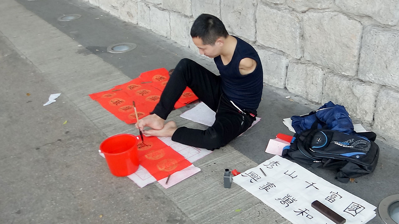 Armless Man Painting with feet on sidewalk in Hong Kong