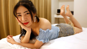 Asian Masseuse Vikki poses on bed in shorts