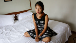 Shy Girl sits on bed in dress