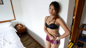 Shy Girl poses against wall in bra and shorts