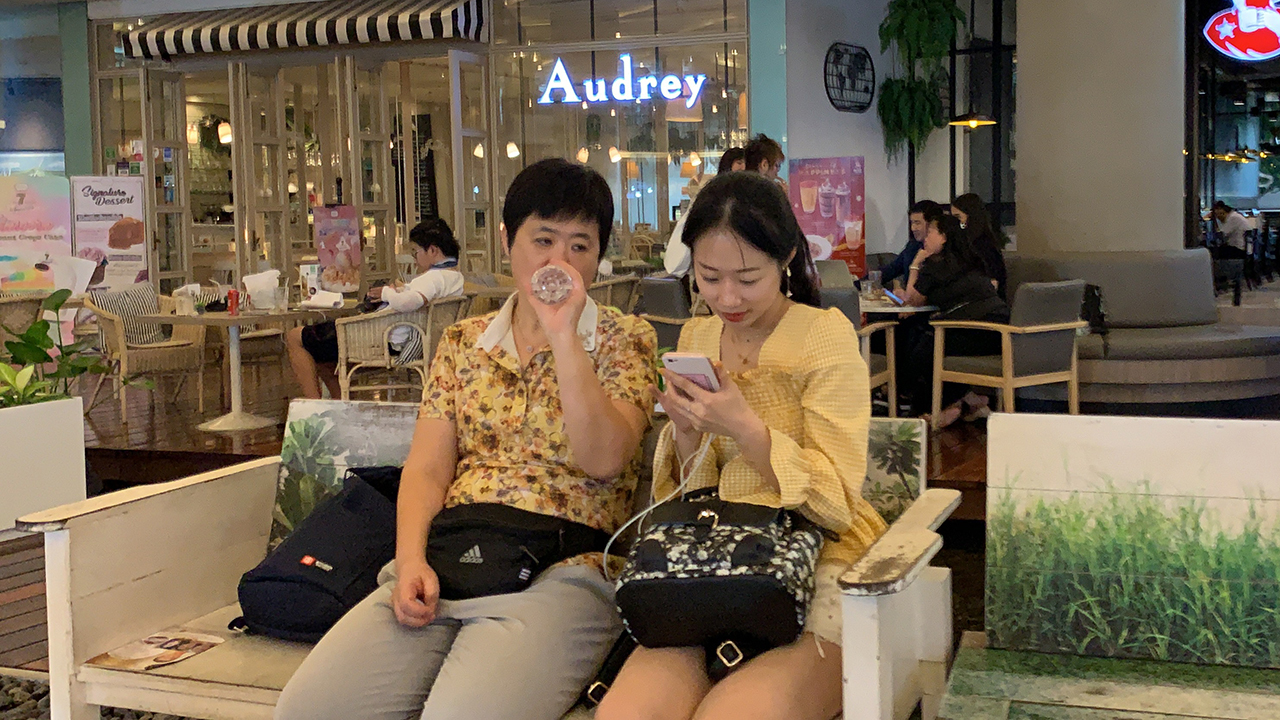 Chinese Tourists sit at mall bench with no masks on