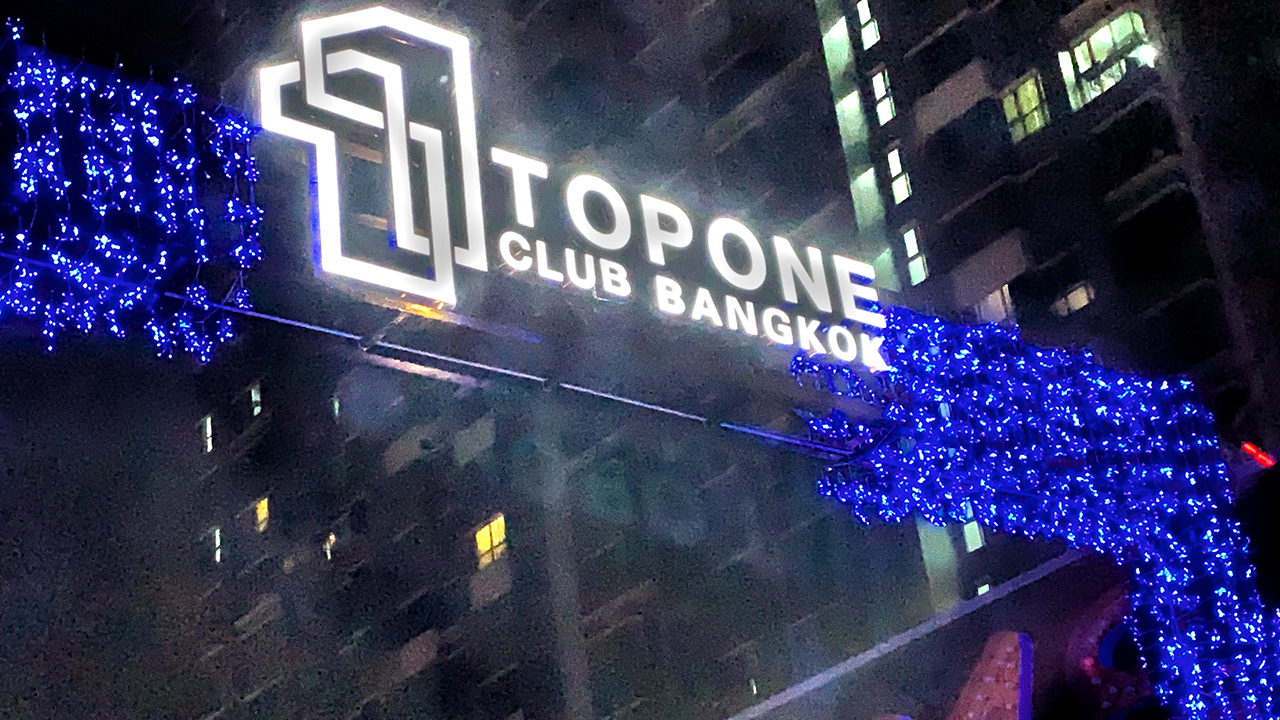 View of Top One Club Bangkok sign above street at night