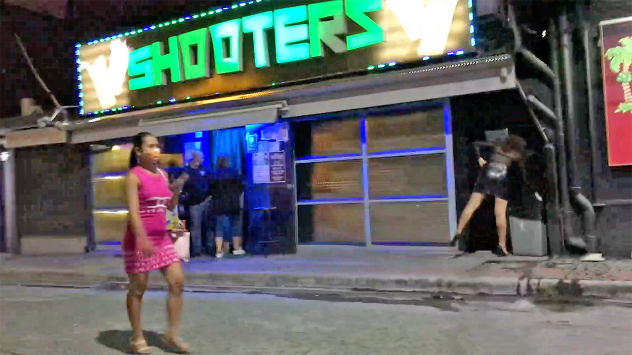 View of Filipina girl wearing mask walking by Shooters Bar Angeles City building facade
