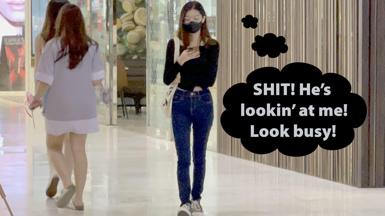 Skinny Thai girl texting while walking in EM Quarter Mall in Bangkok